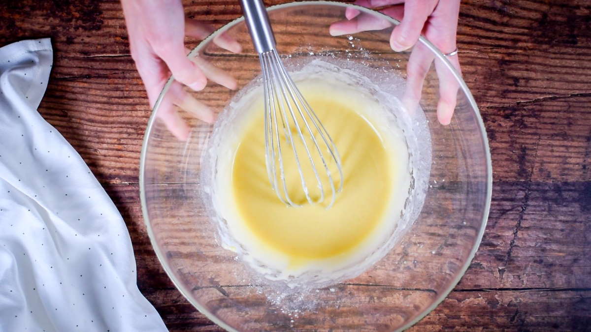 Cake batter in a bowl with a whisk. Measuring spoons on the side.