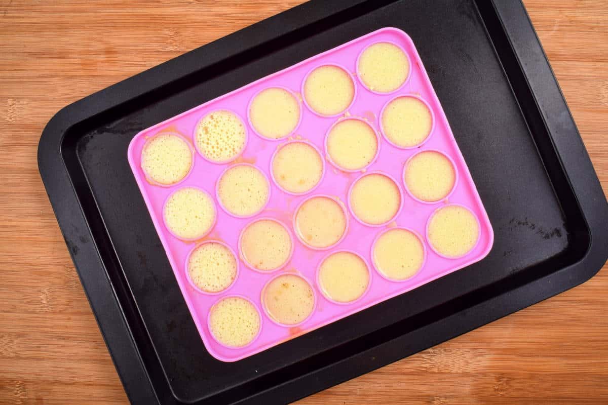 Cake pop mold with batter in it on sheet pan, wooden background.