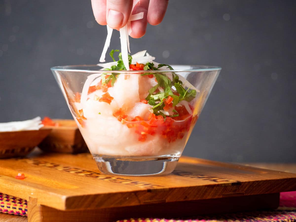 Ceviche in a glass bowl with onion, cilantro and red chili peppers.