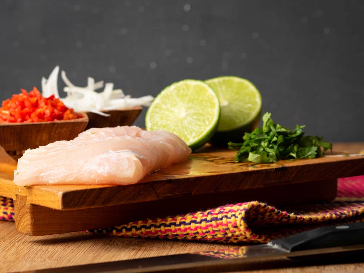 Raw fish, limes, onions, hot peppers and cilantro prepped on cutting board.