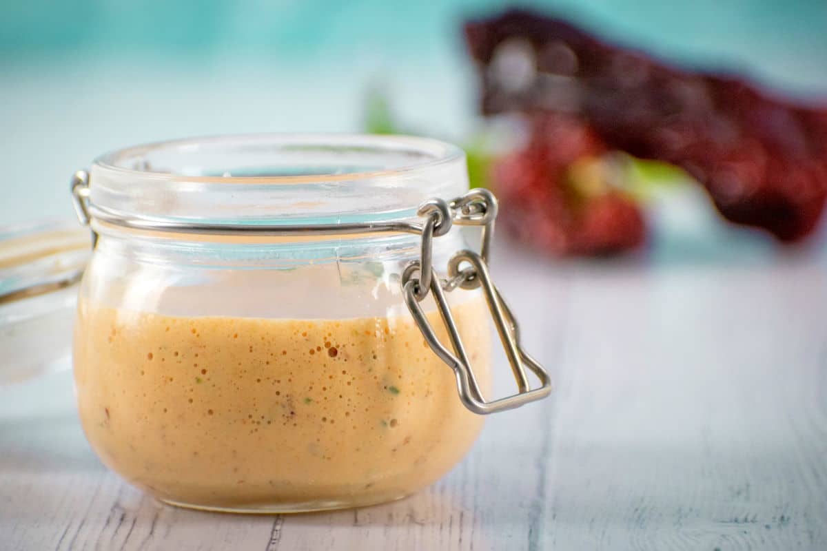 Chipotle sauce in a jar on blue background, peppers in the background.