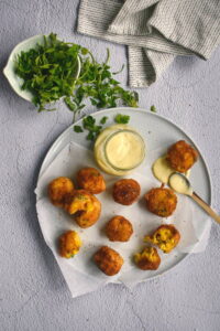 A plate of corn nuggets with dipping sauce, cilantro on the side.