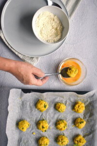 Raw corn nuggets on a wax paper lined baking sheet, bowls of egg and flour on the side.