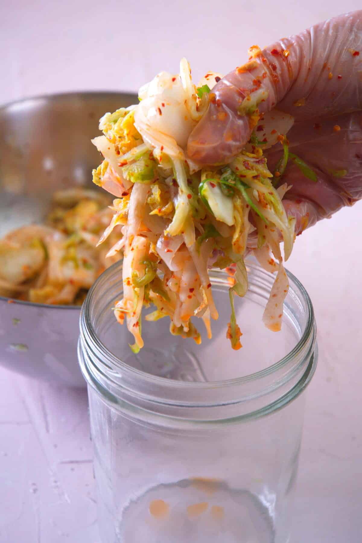 A hand holding kimchi over a jar.