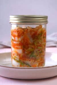 Kimchi in a sealed jar in a white dish.