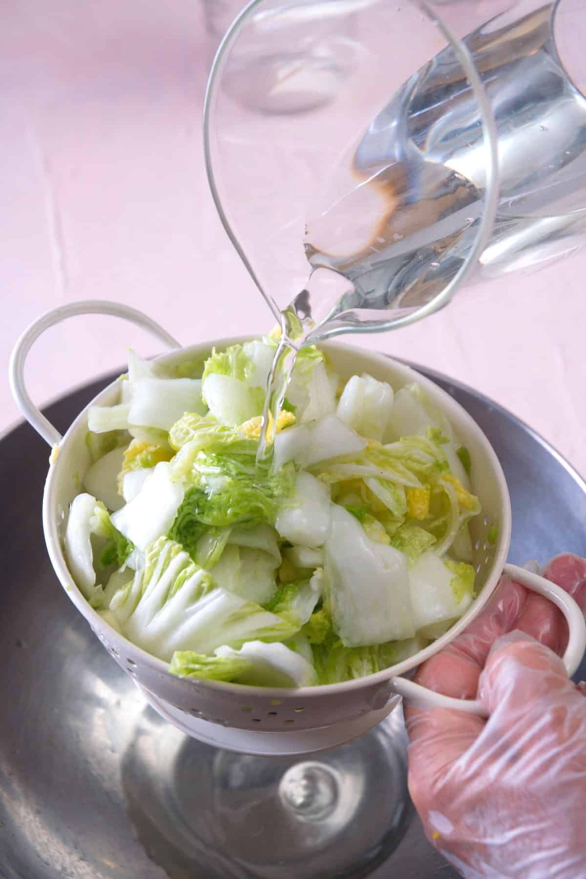 Chopped Napa cabbage in a colander with water running over it.