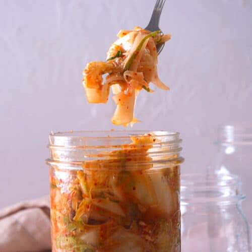 Kimchi on a fork over a jar.
