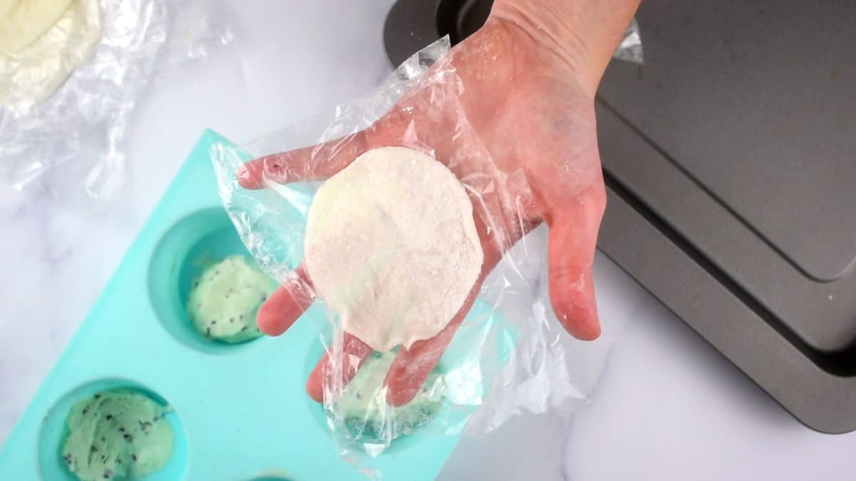 Mochi dough circle on plastic wrap in a hand.