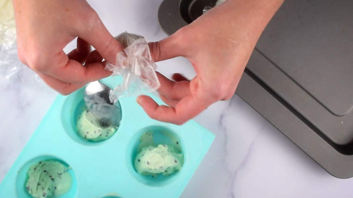Hands tying up mochi ice cream ball in plastic wrap.