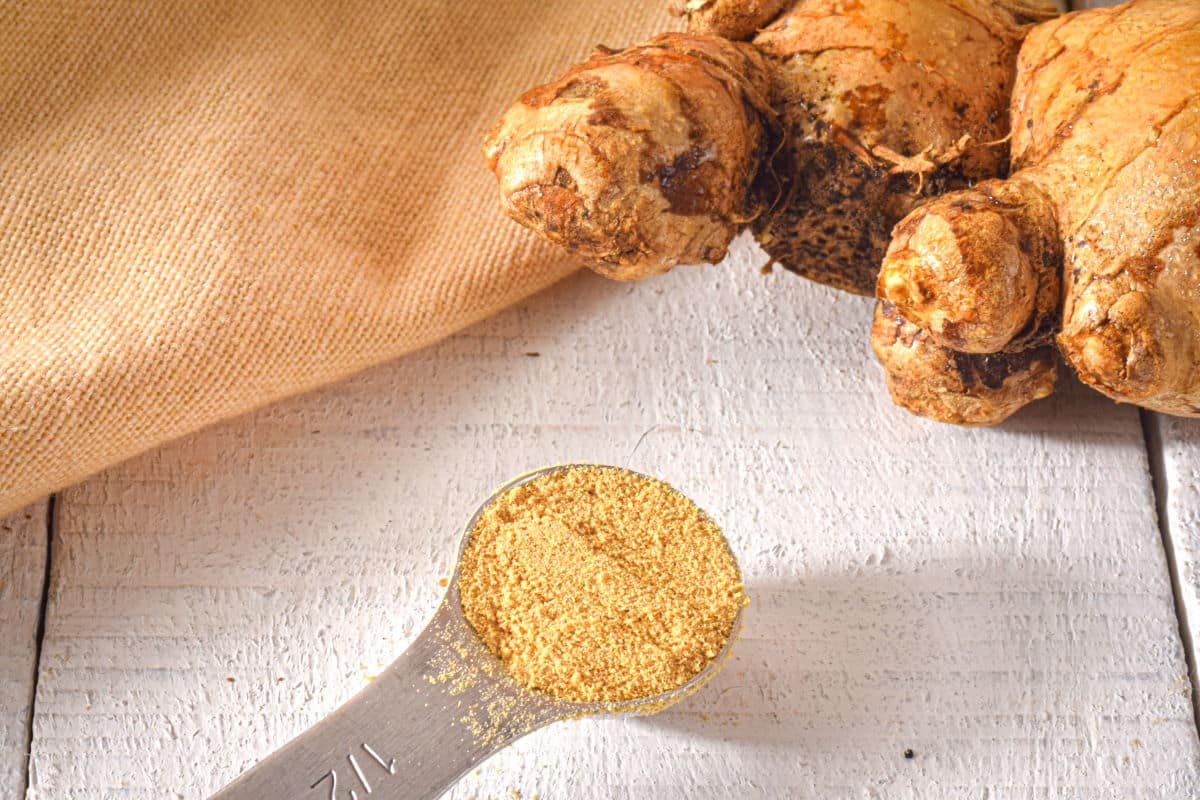 Ground and fresh ginger on white, wooden background.