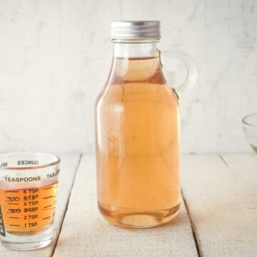 A glass bottle of simple syrup, a small measuring glass on the side.