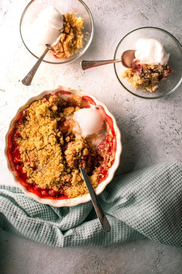 Strawberry crumble in a tart dish and dessert bowls, light background.
