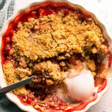 Overhead view of strawberry crumble in white tart dish with a light blue kitchen towel on the side.