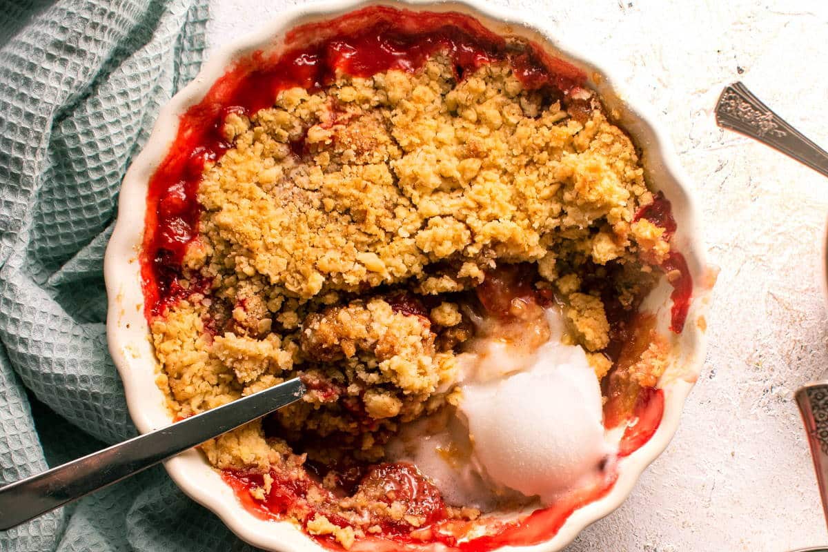 Overhead view of strawberry crumble in white tart dish with a light blue kitchen towel on the side.