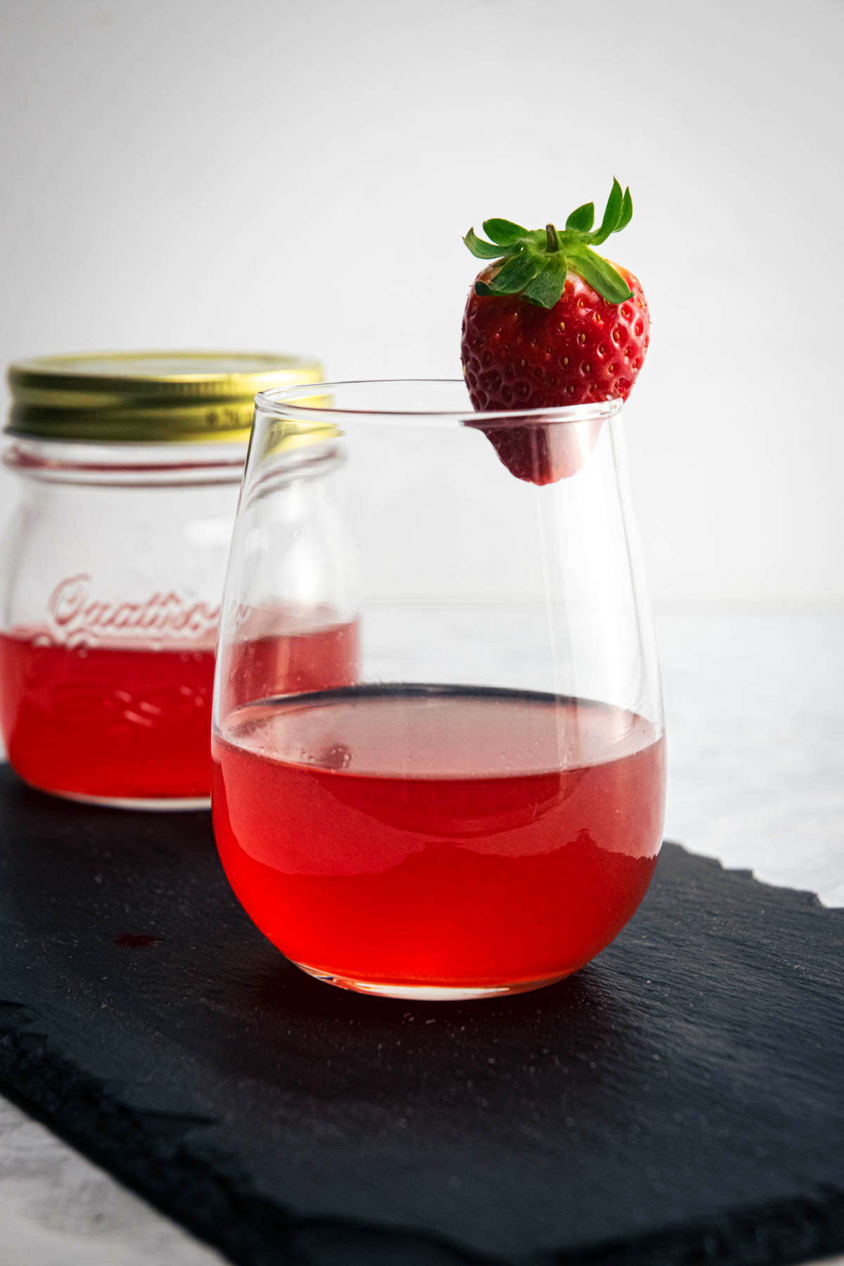 Strawberry liqueur in a jar and wine glass, fresh strawberry on the side.