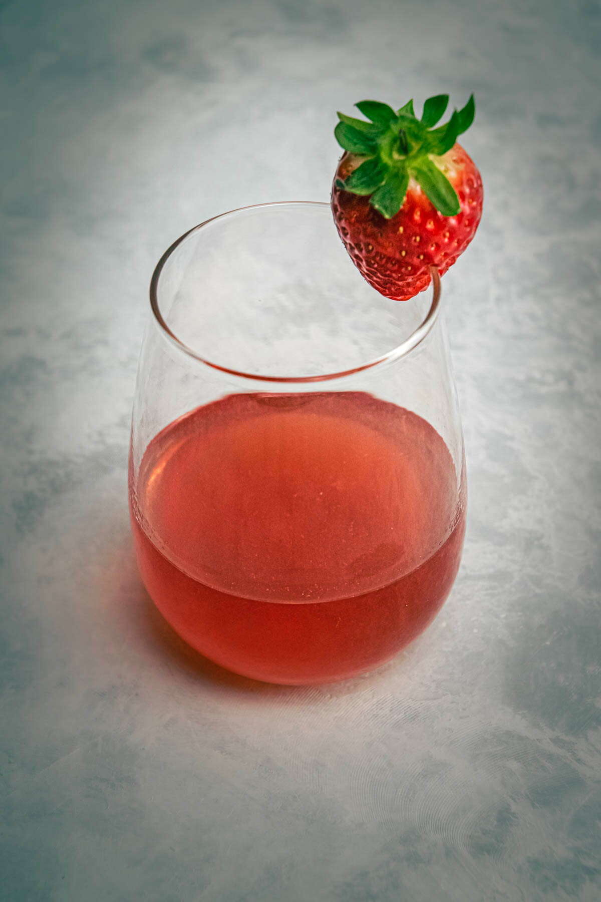 Strawberry liqueur in a wine glass, fresh strawberry on the side.