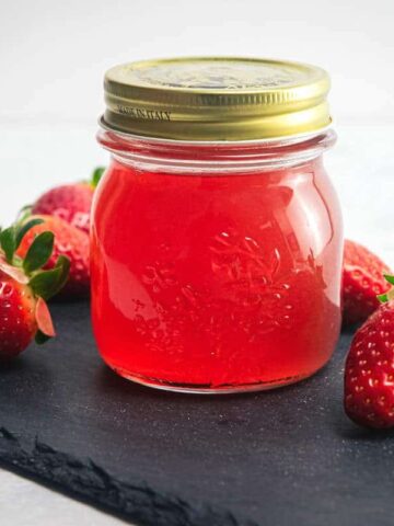 Strawberry liqueur in a jar, fresh strawberries on the side.