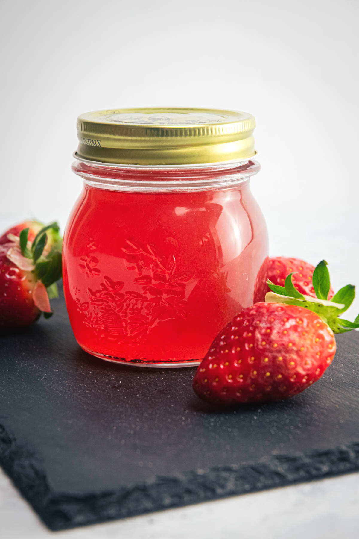 Strawberry liqueur in a jar with fresh strawberries on the side on black serving board.