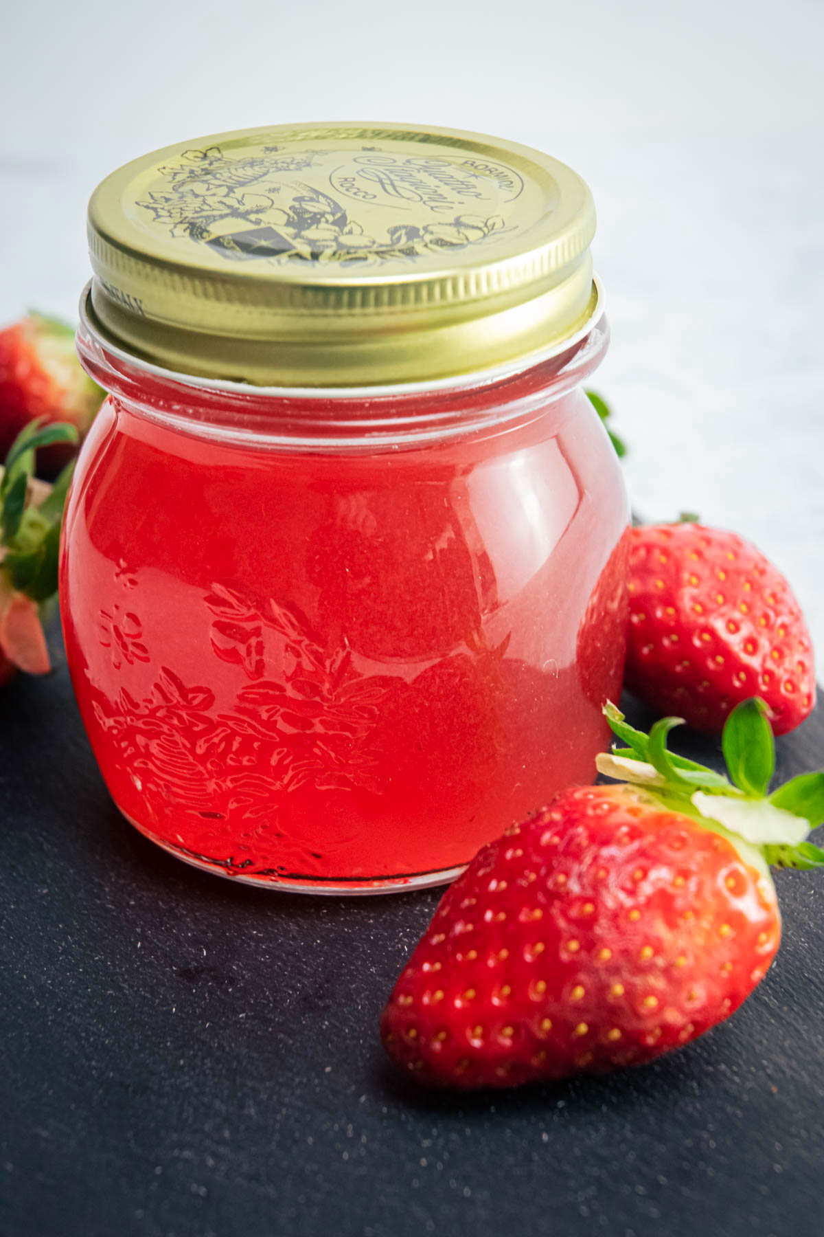 Strawberry liqueur in a sealed jar, with fresh strawberries on the side.