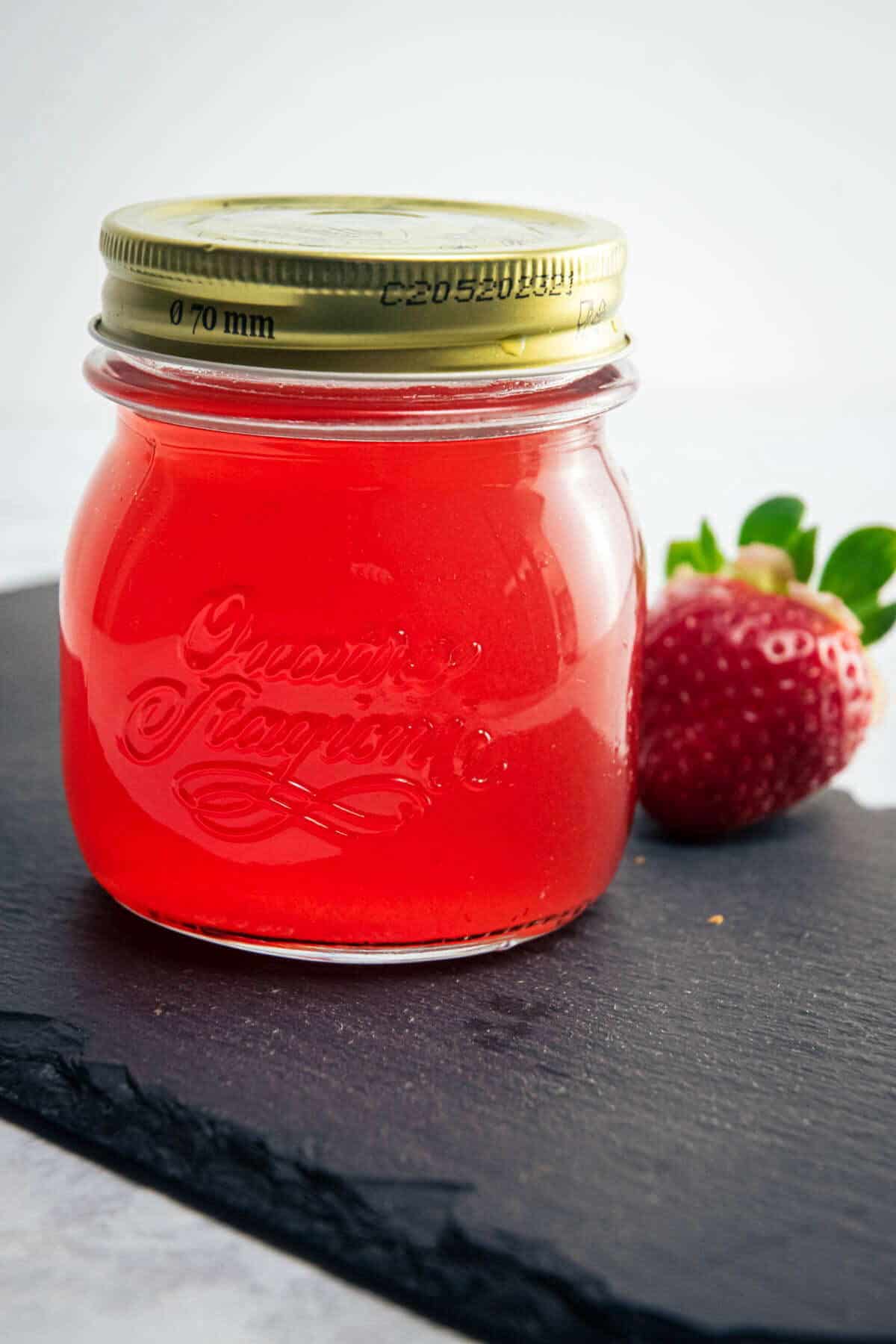 Strawberry liqueur in a jar, fresh strawberry on the side.
