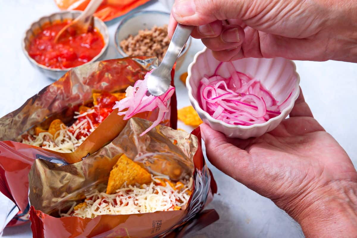 Open Dorito bags with taco filling and a small bowl of pickled red onions.