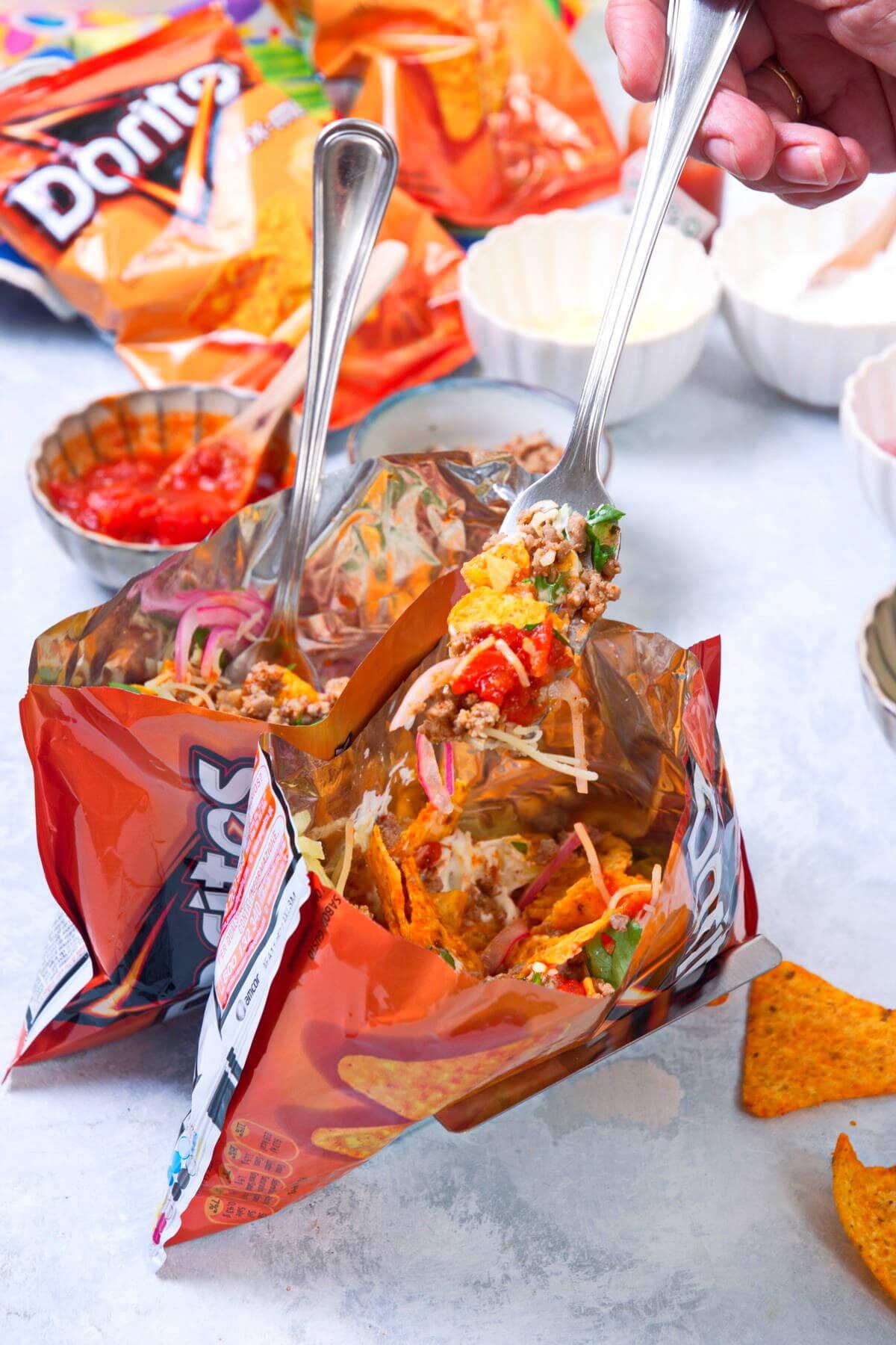 Taco in a bag with forks and toppings in the background.