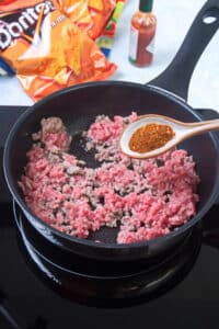 Ground beef in a pan with taco seasoning on a spoon.