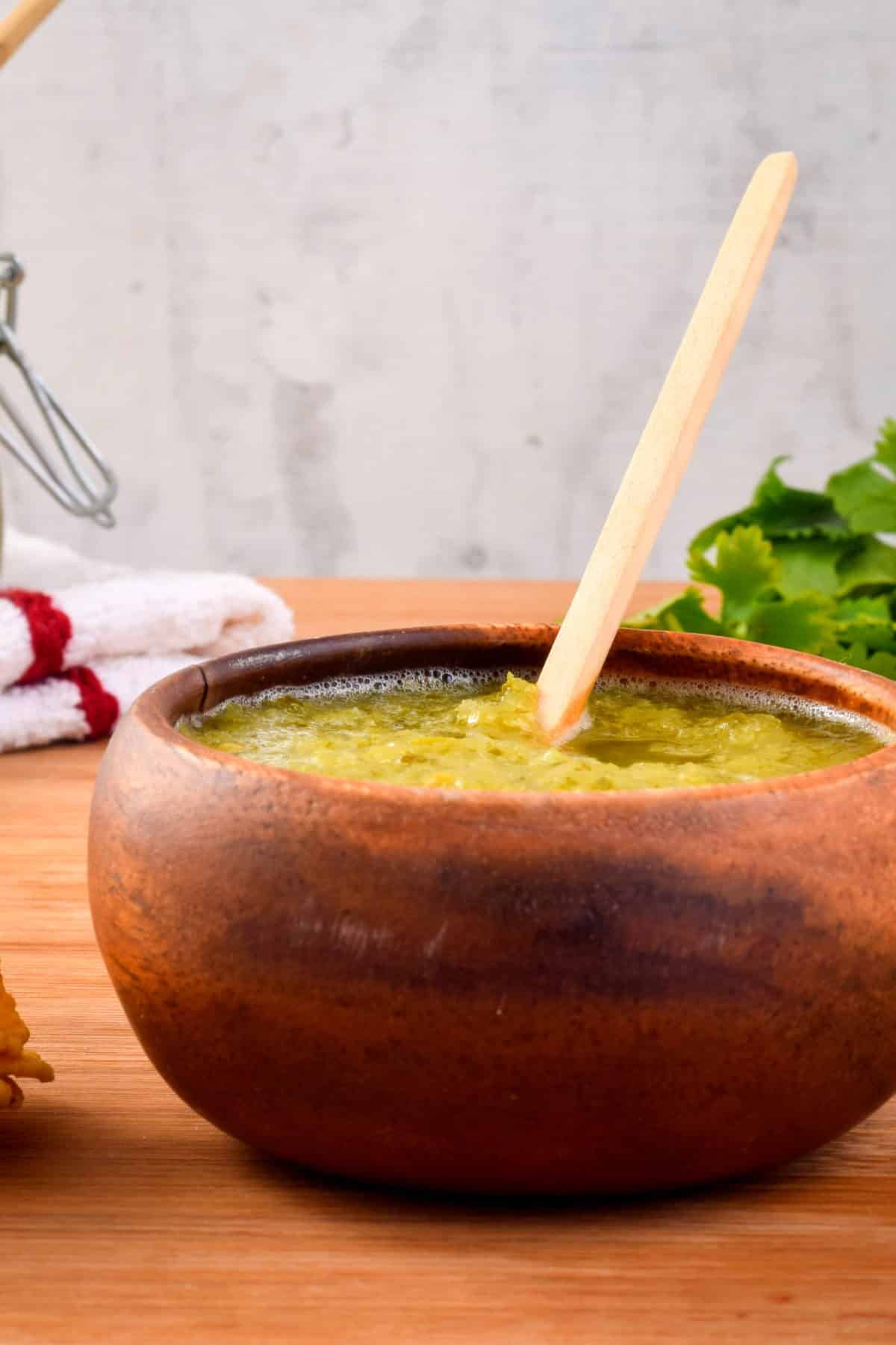 A wooden bowl of tomatillo salsa, cilantro in the background.