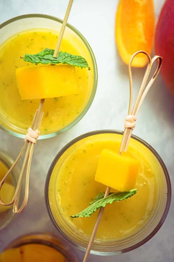 Mango pineapple smoothies in 2 glasses with mango and mint skewers.