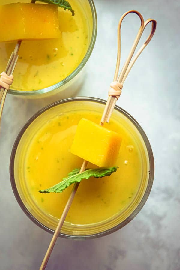 Mango pineapple smoothies in 2 glasses with mango and mint skewers.