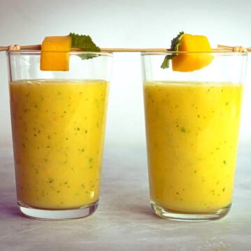 Mango pineapple smoothies in 2 glasses with mango and mint skewers.