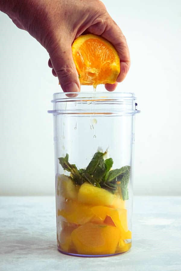 Mango pineapple smoothie ingredients in a jar with a freshly squeezed orange.