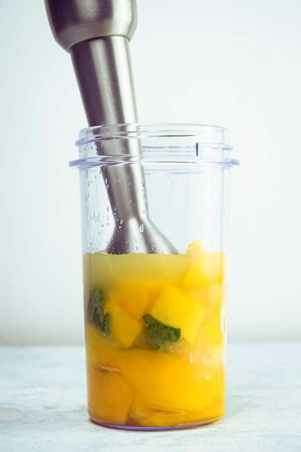 Mango pineapple smoothie and a blender, white background.