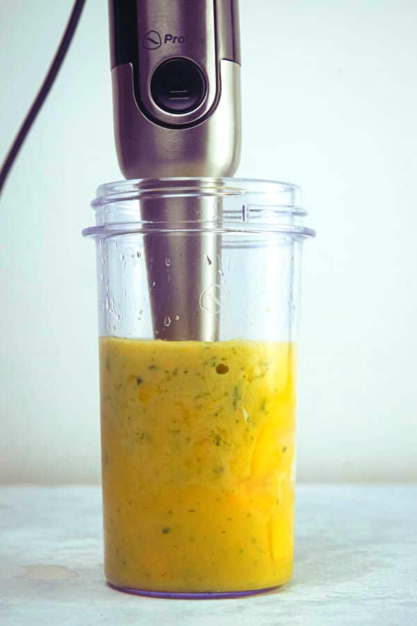Mango pineapple smoothie and a blender, white background.