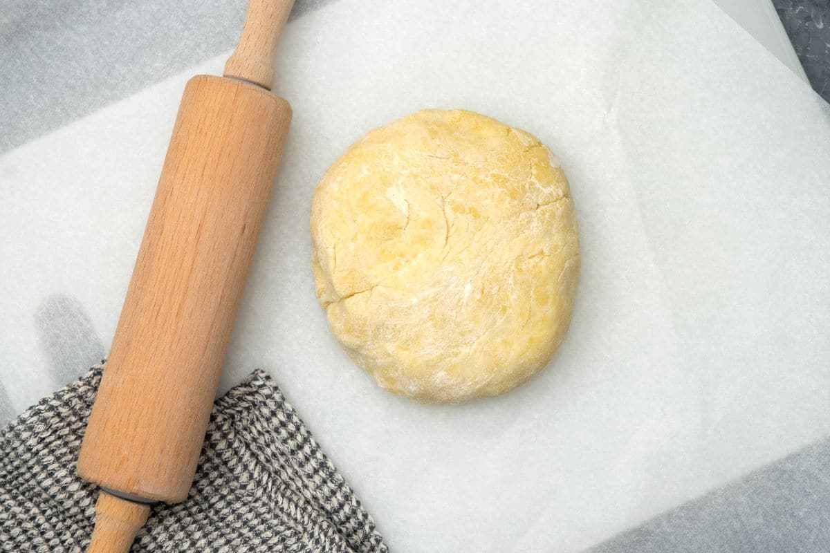 Pastry dough on parchment paper with a rolling pin.
