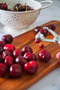 Cherries and cherry pitter on cutting board.