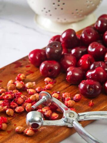 Pitted cherries and a cherry pitter on cutting board.