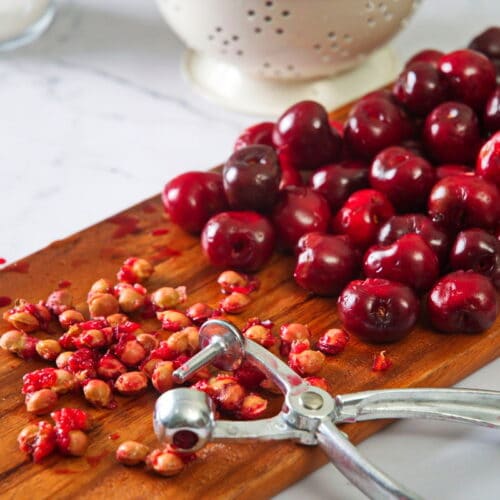 Pitted cherries and a cherry pitter on cutting board.