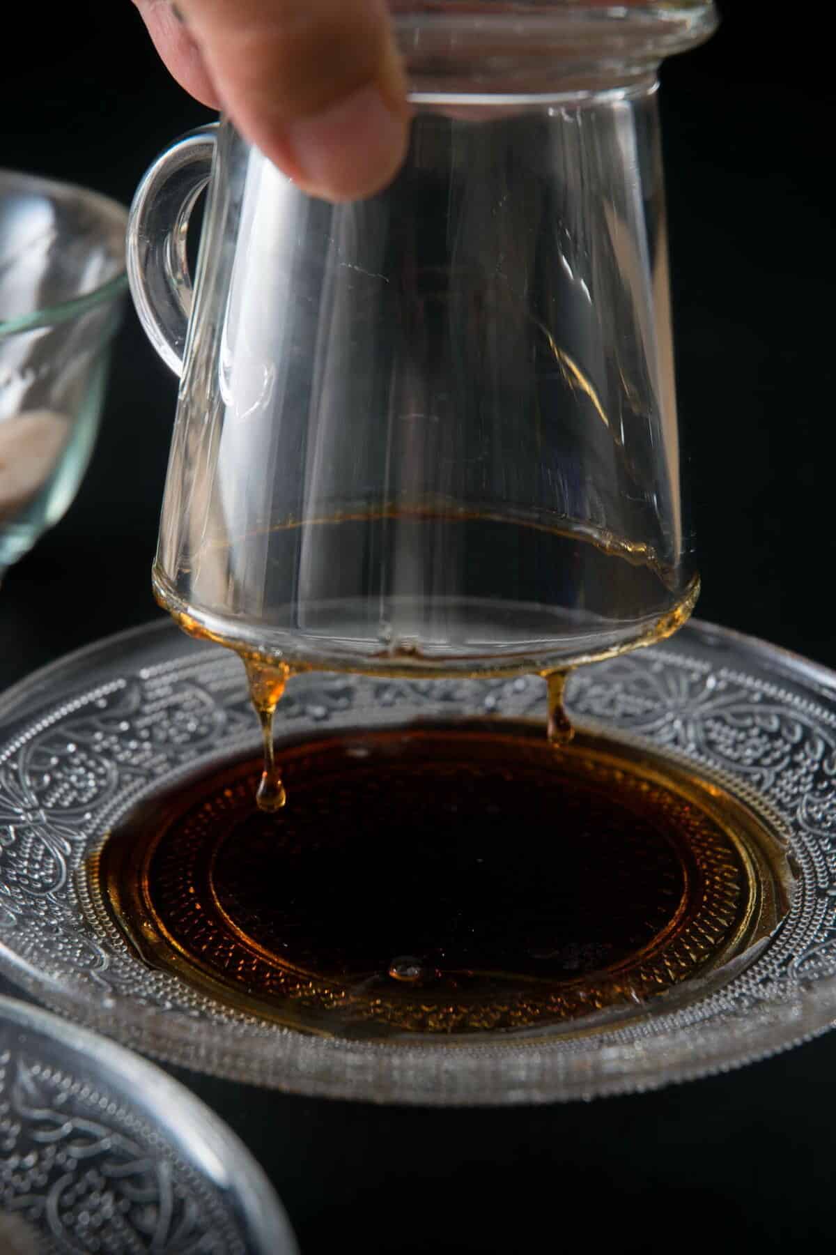 A clear glass coffee mug dipped into a plate of maple syrup.