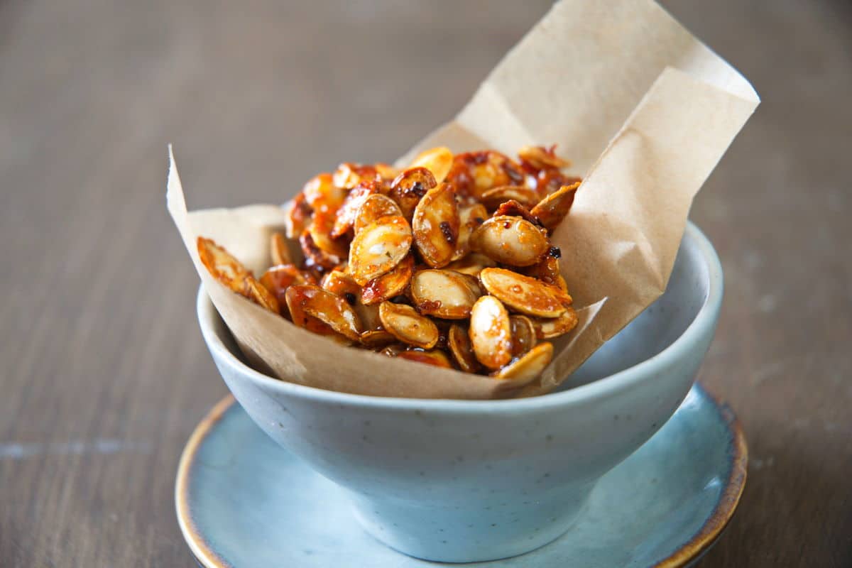 Roasted butternut squash seeds in a small blue bowl with parchment paper.