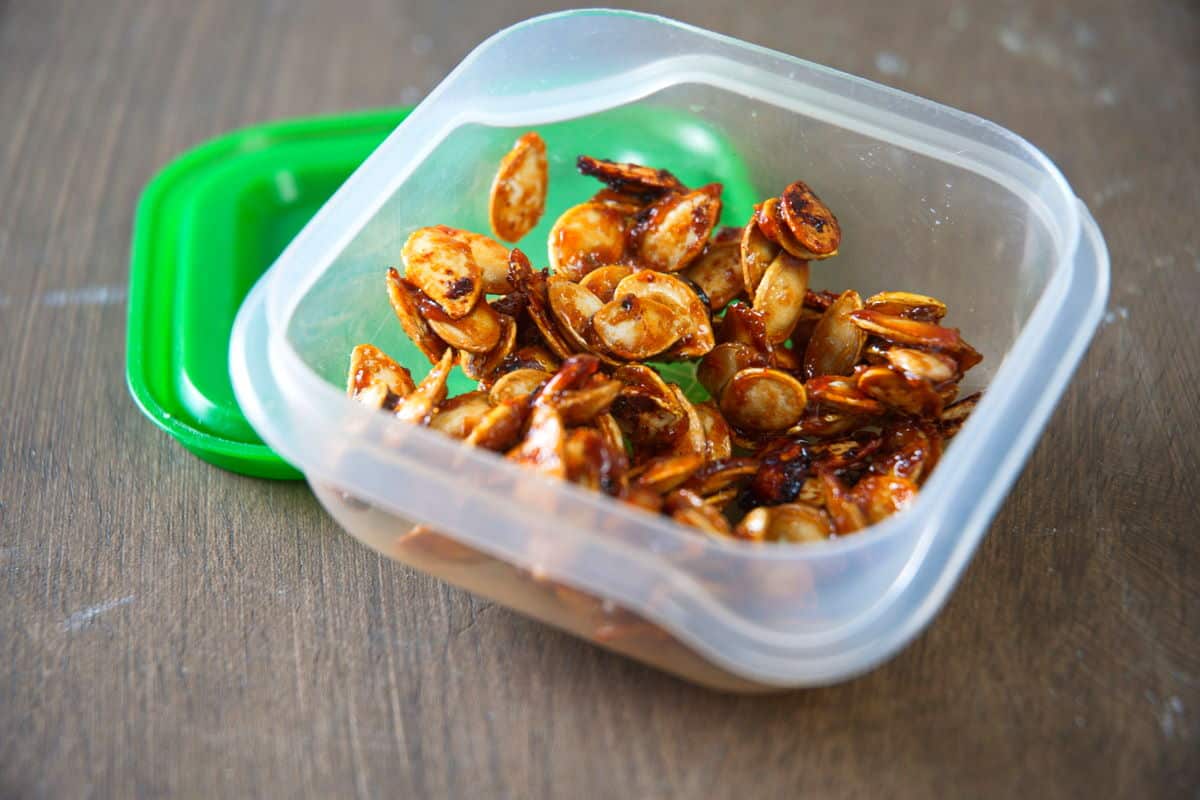 Roasted butternut squash seeds in a small container with green lid.