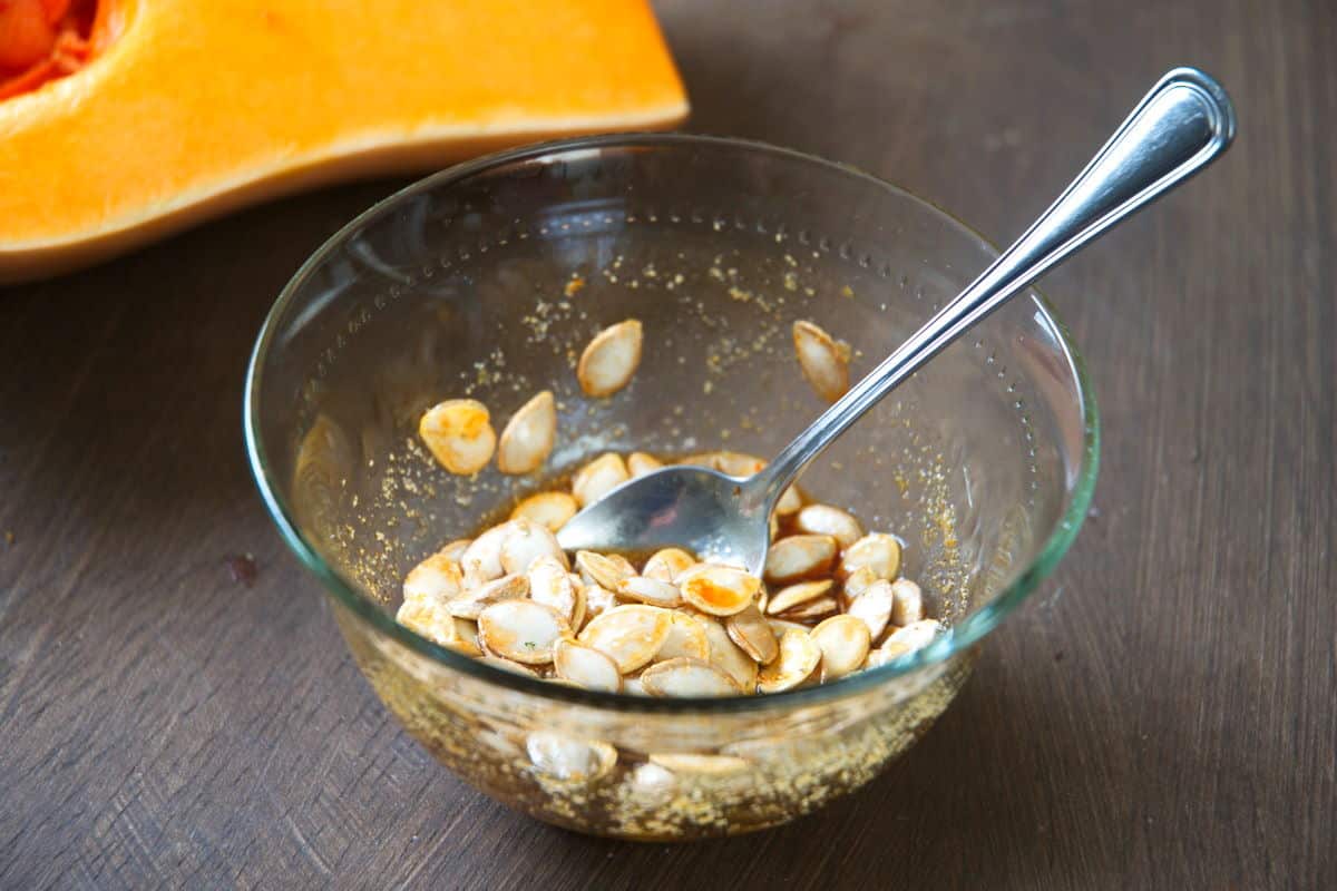 Butternut squash seeds in a bowl with a brown sugar and soy mixture.
