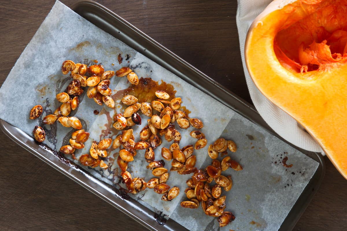 Roasted butternut squash seeds on a parchment paper lined sheet pan.