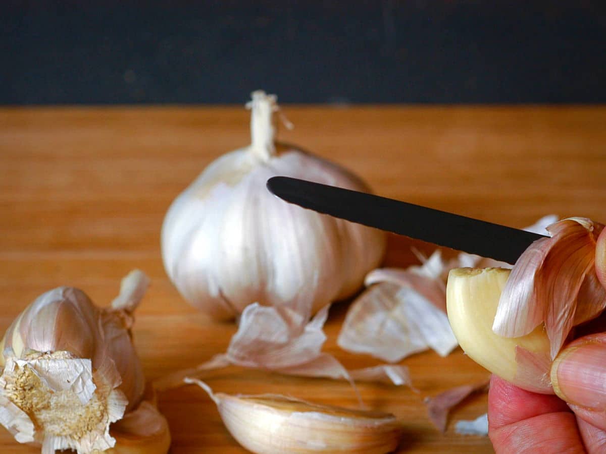 Garlic clove skin getting peeled with small knife.