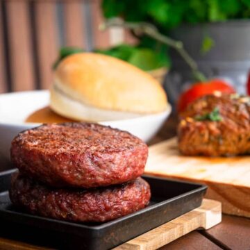 Cooked burger patties on a cast iron pan, on wooden table.