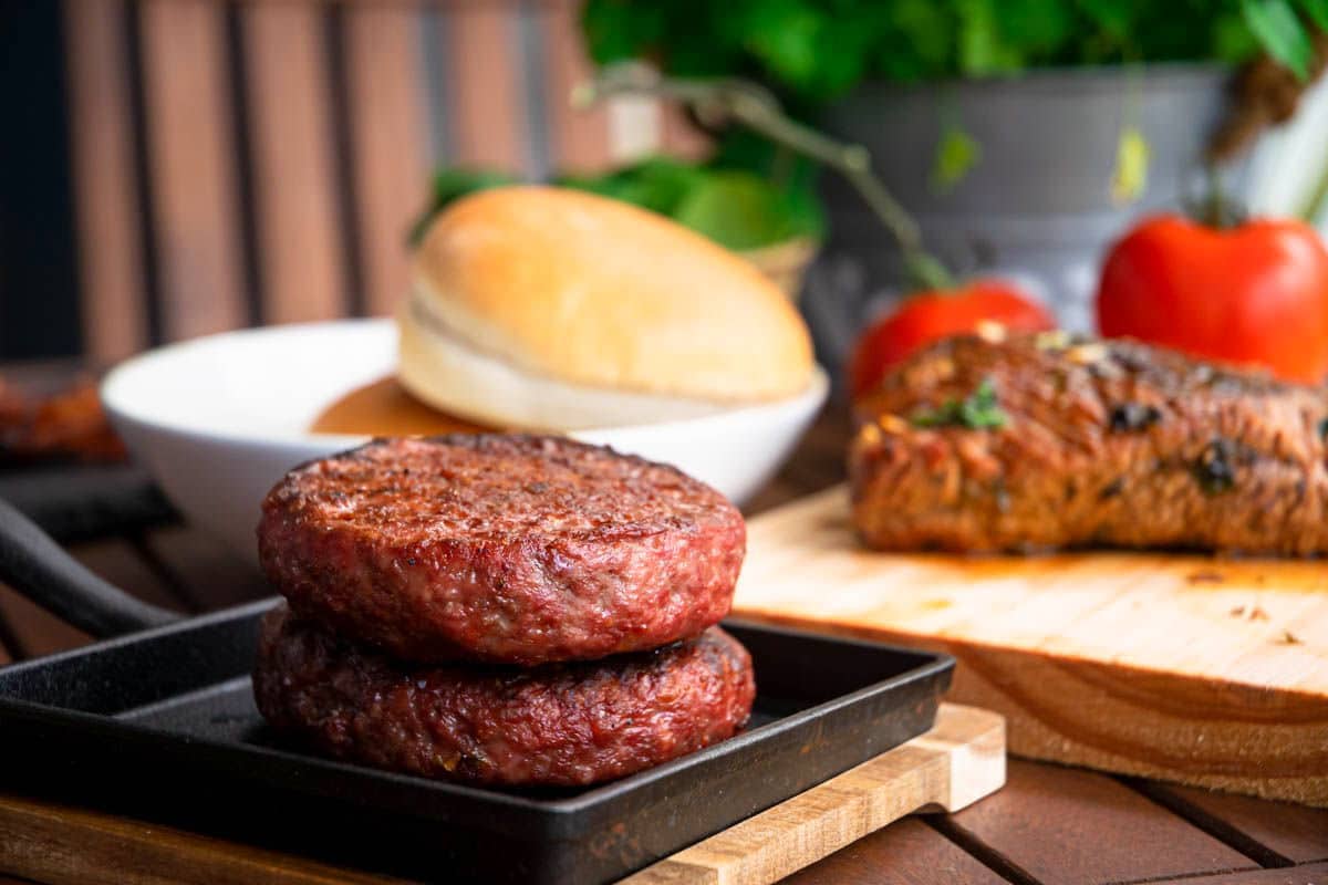 Cooked burger patties on a cast iron pan, on wooden table.