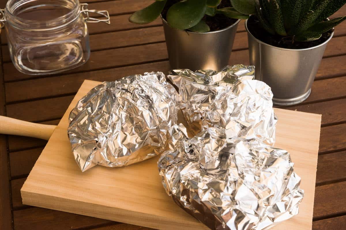 Foil wrapped bell peppers on a wooden board.