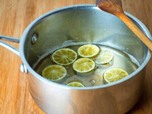 Candied limes in a pot with a wooden spoon, wooden background.