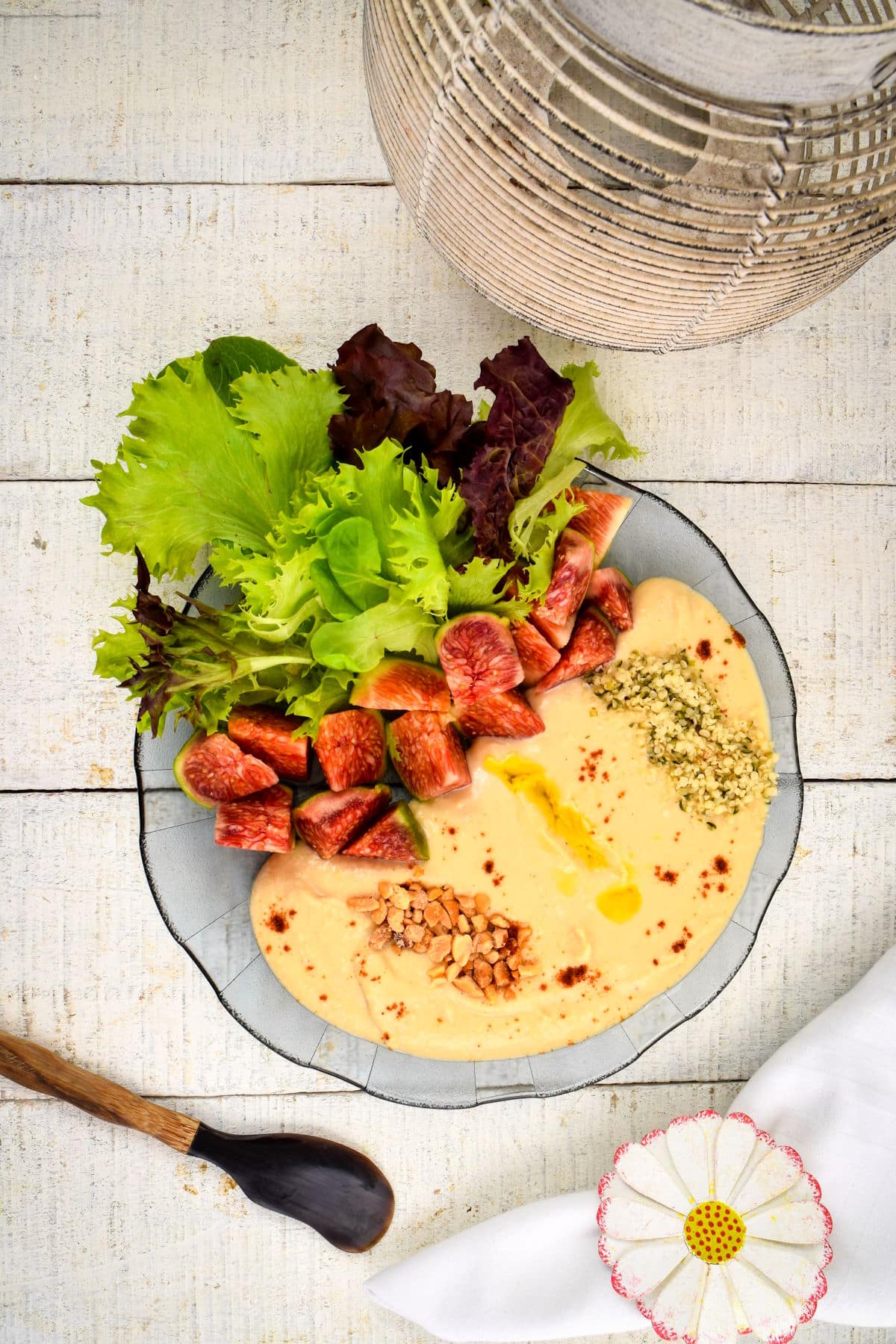 Hummus dip in a bowl with fresh lettuce, figs, nuts, hemp seeds and olive oil.