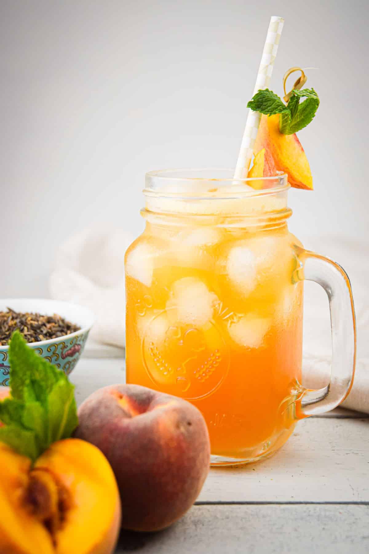 Iced peach green tea in glass with ice, straw and peach garnish.